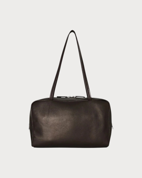 The Row Astra bowling bag in dark brown lambskin leather with dual zipper closure and elongated handles.