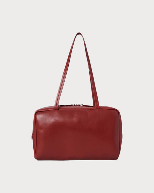 The Row Astra bowling bag in barn red lambskin leather with dual zipper closure and elongated handles.